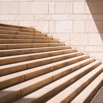 A small child sitting at the foot of a large staircase