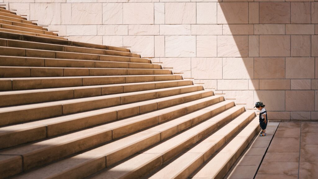 A small child sitting at the foot of a large staircase