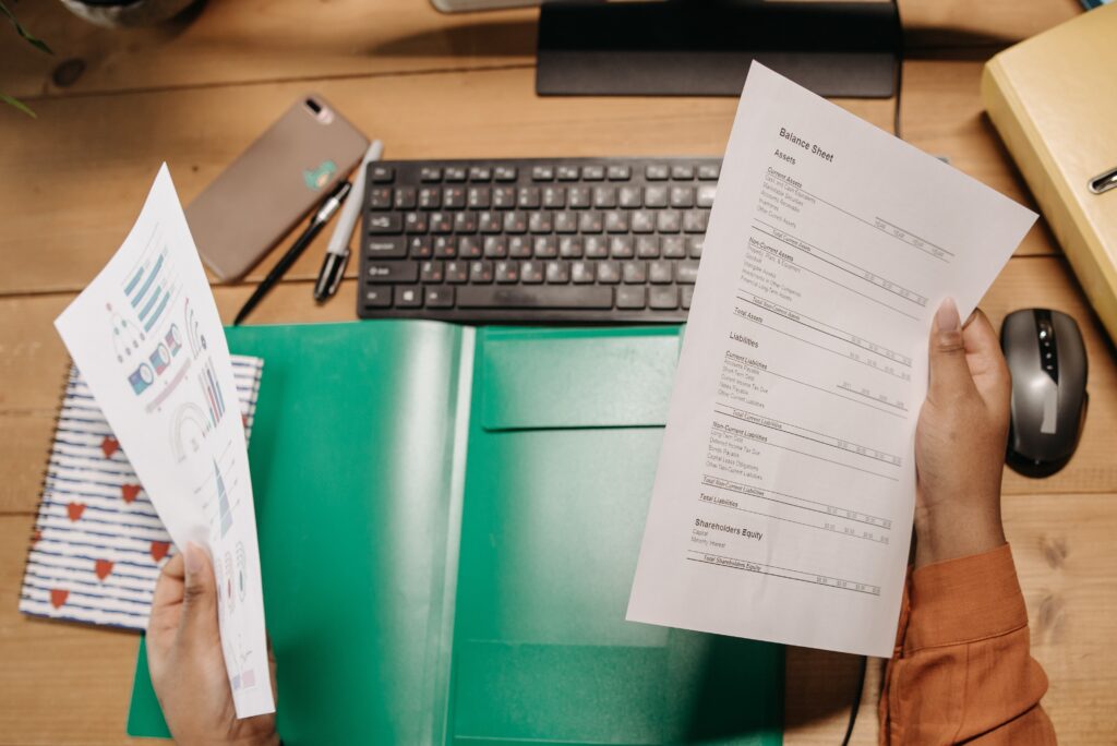 A person holding a balance sheet above their computer