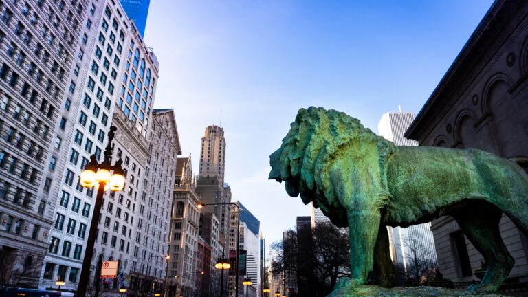 A side view of a row of buildings in Chicago with a lion statue in the foreground