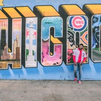 A person standing in front of street art reading "Greetings from Chicago"