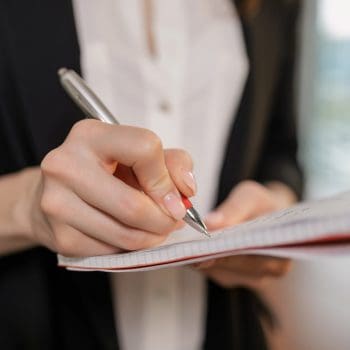 Close-up of a person writing with a pen on a notepad