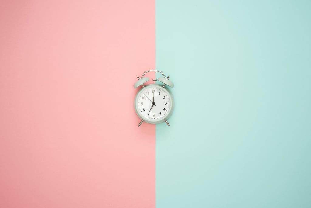 An alarm clock against a pink and blue background