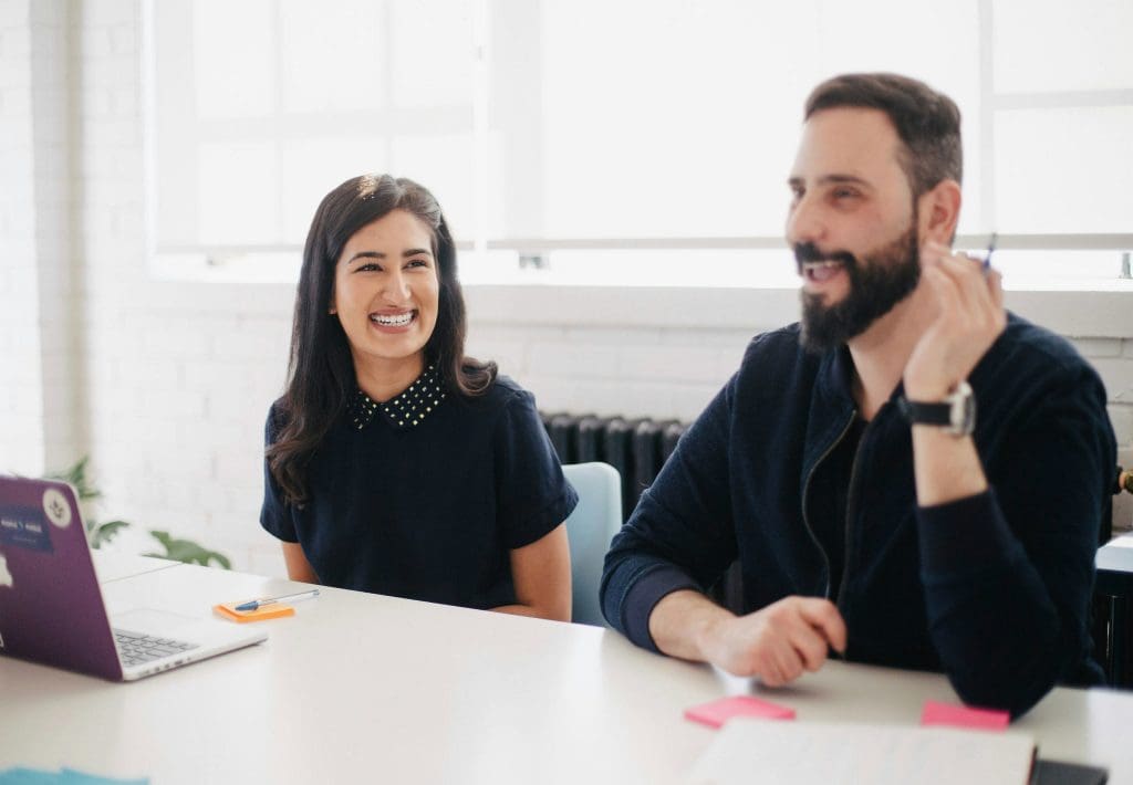 A male and female coworker sitting at a desk smiling and laughing