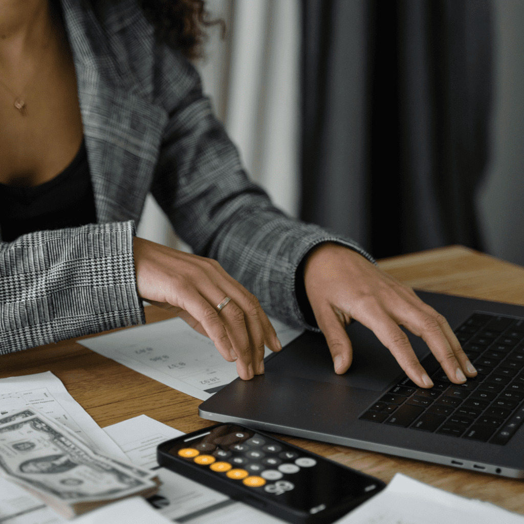 A woman using a laptop with a calculator and money next to her